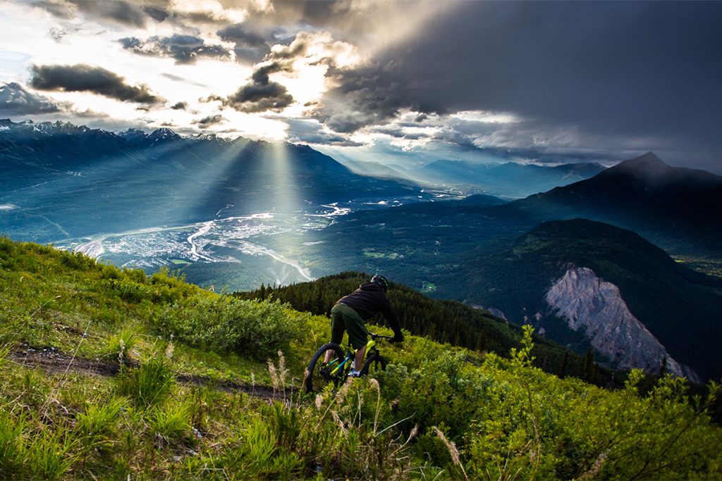 Mountain biker riding downhill as sun rays appear over the valley