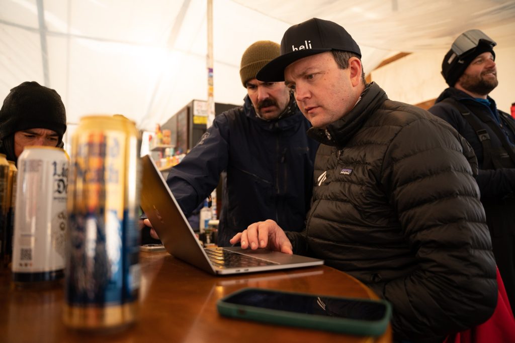 Two males dressed in ski gear working on a computer in a urt